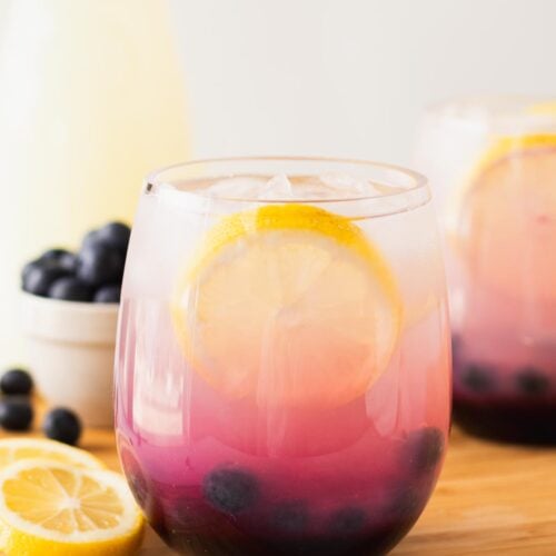 Pretty blueberry lemonade in a glass with lemon wedge and fresh blueberry garnish.