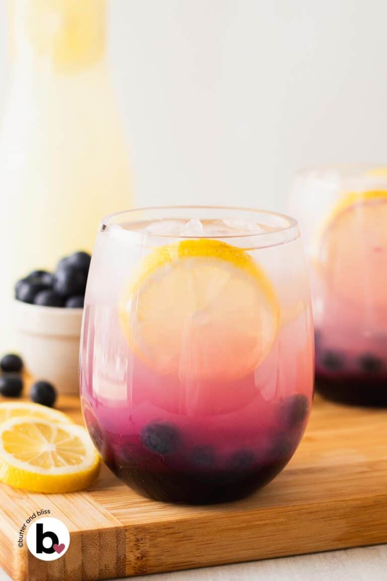 Pretty blueberry lemonade in a glass with lemon wedge and fresh blueberry garnish.