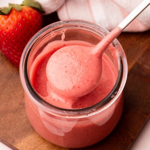 Fresh strawberry glaze being lifted out of a small jar on a spoon.