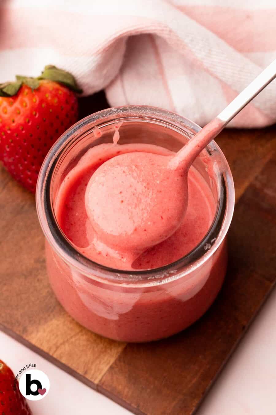 Fresh strawberry glaze being lifted out of a small jar on a spoon.