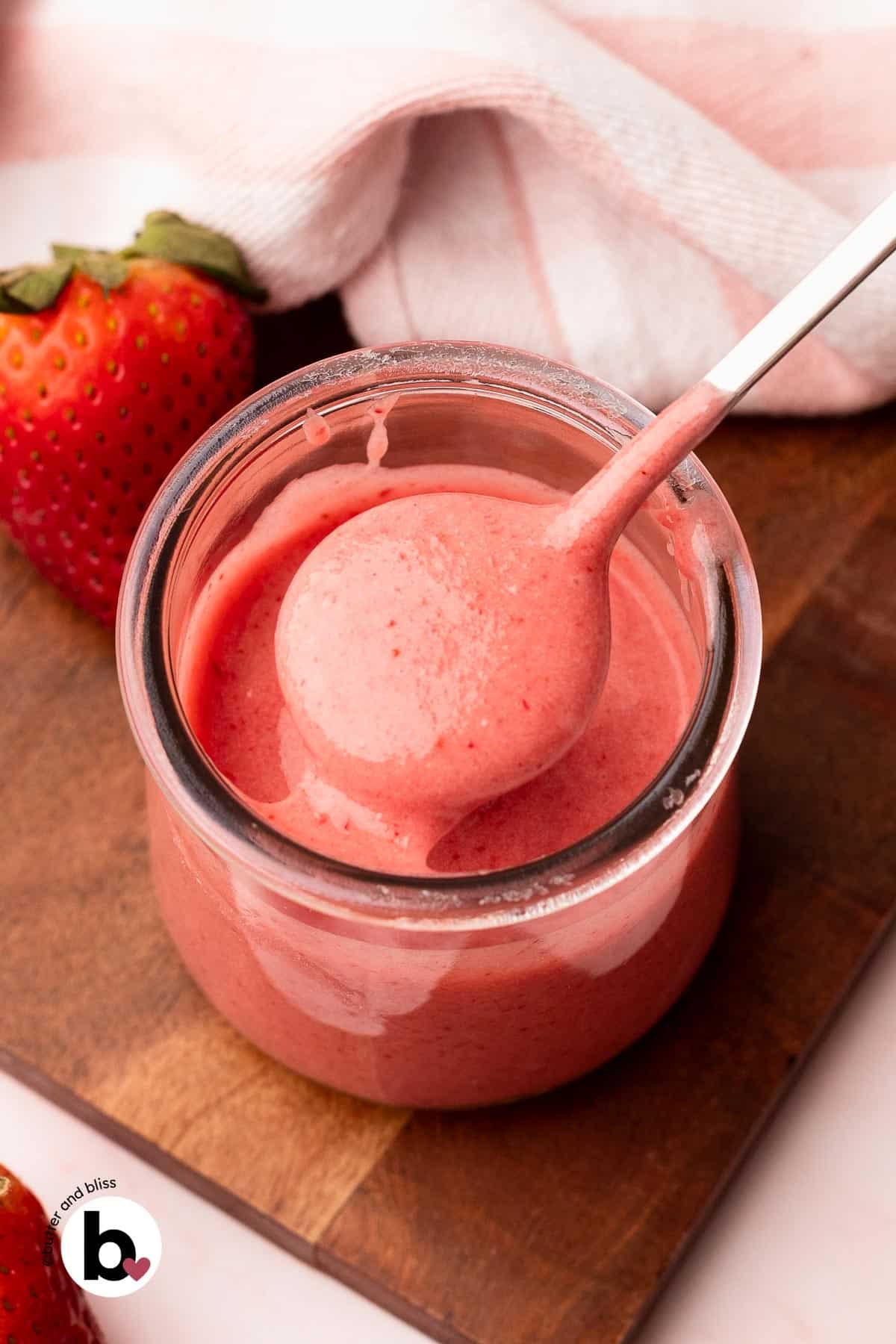 Fresh strawberry glaze being lifted out of a small jar on a spoon.