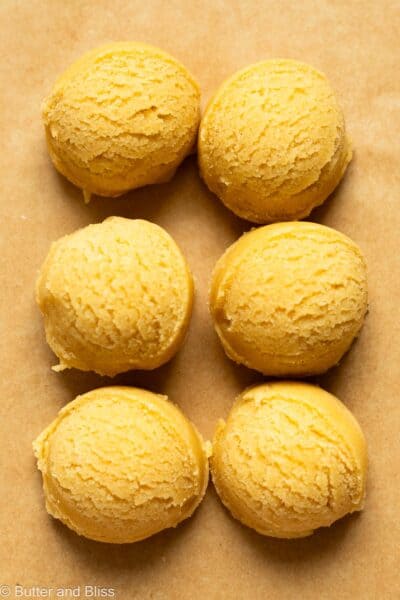 Six portioned sugar cookie dough balls on a piece of parchment.