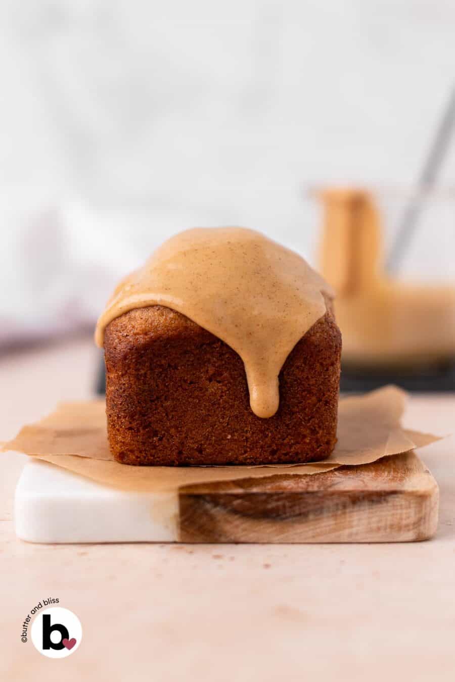 Individual apple banana bread loaf with drippy icing on a small marble plate.