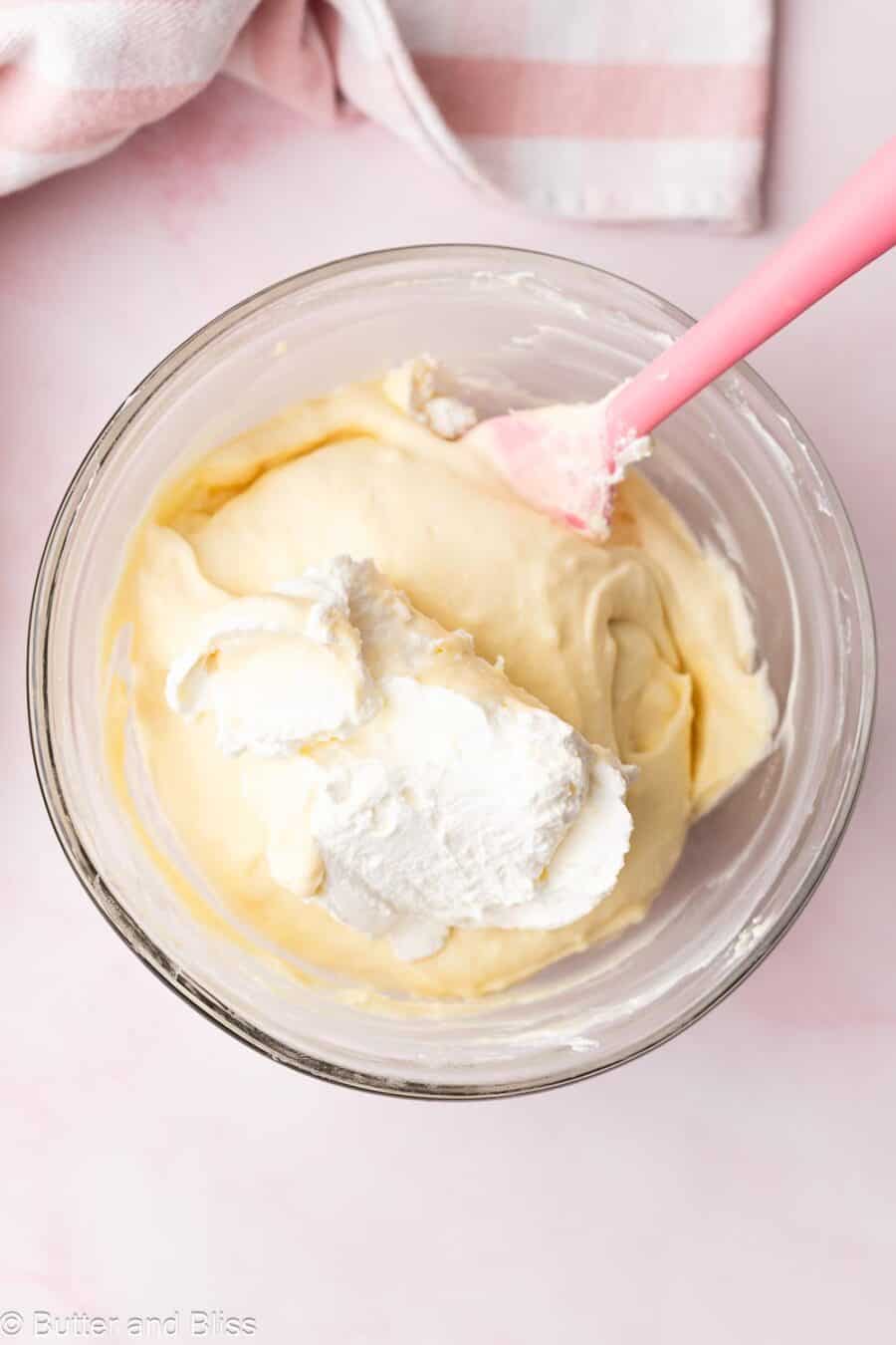 Whipped cream being folded into vanilla pudding in a mixing bowl.