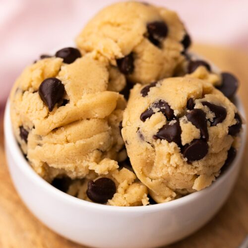 Scoops of edible chocolate chip cookie dough in a small whilte bowl with a pink napkin.