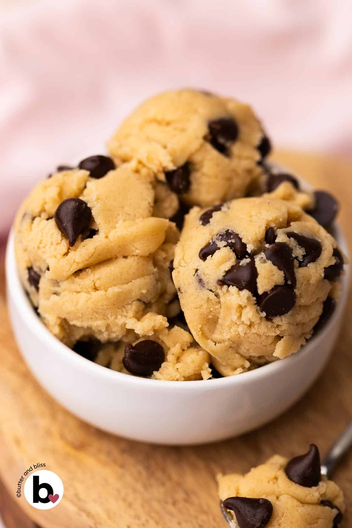 Scoops of edible chocolate chip cookie dough in a small whilte bowl with a pink napkin.