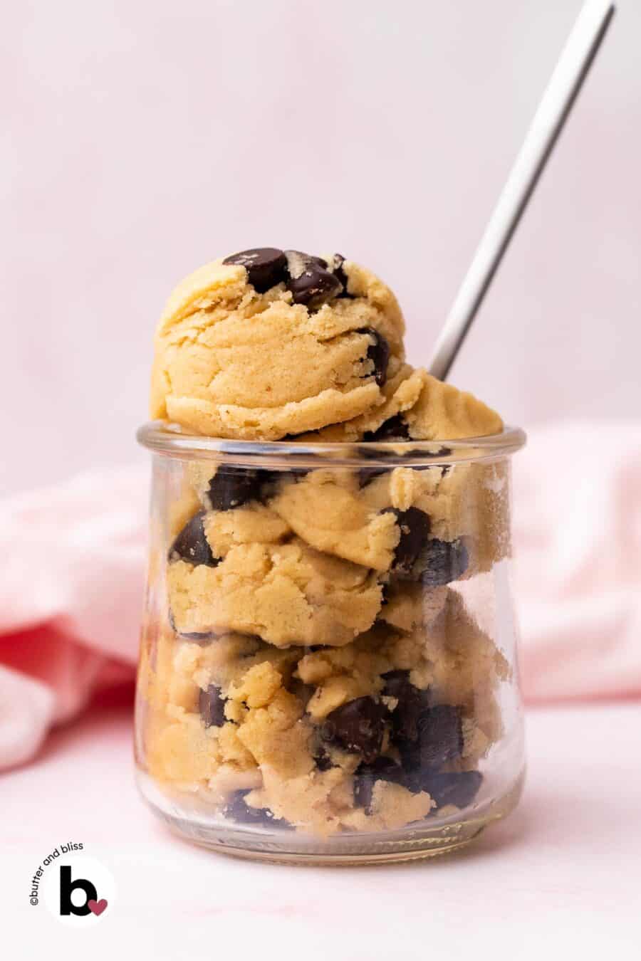A small jar of edible chocolate chip cookie dough with a spoon and pink napkin by Butter and Bliss.