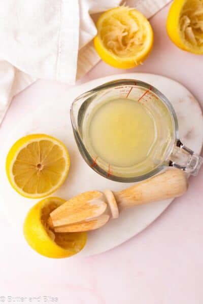 Fresh squeezed lemon juice in a measuring cup with squeezed lemons next to it.