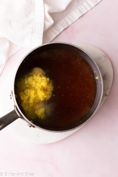 Grated ginger added to honey simple syrup in a saucepan.