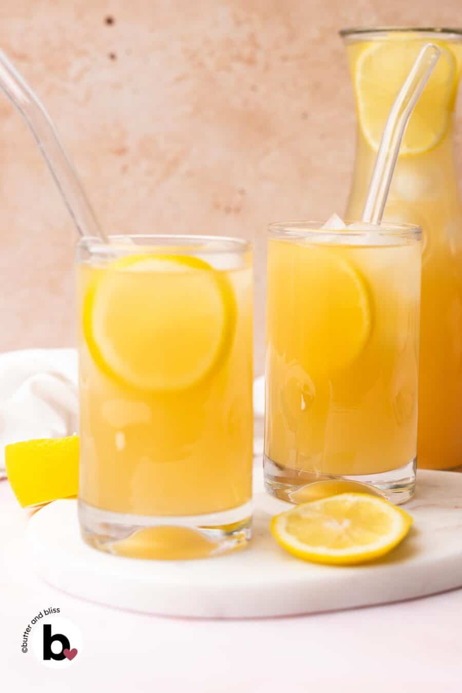 Two glasses of ginger lemonade garnished with a lemon slice on a marble plate.