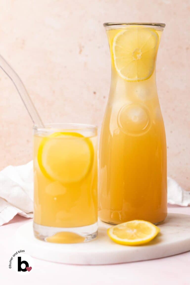 A glass of ginger lemonade next to a pitcher on a marble plate.