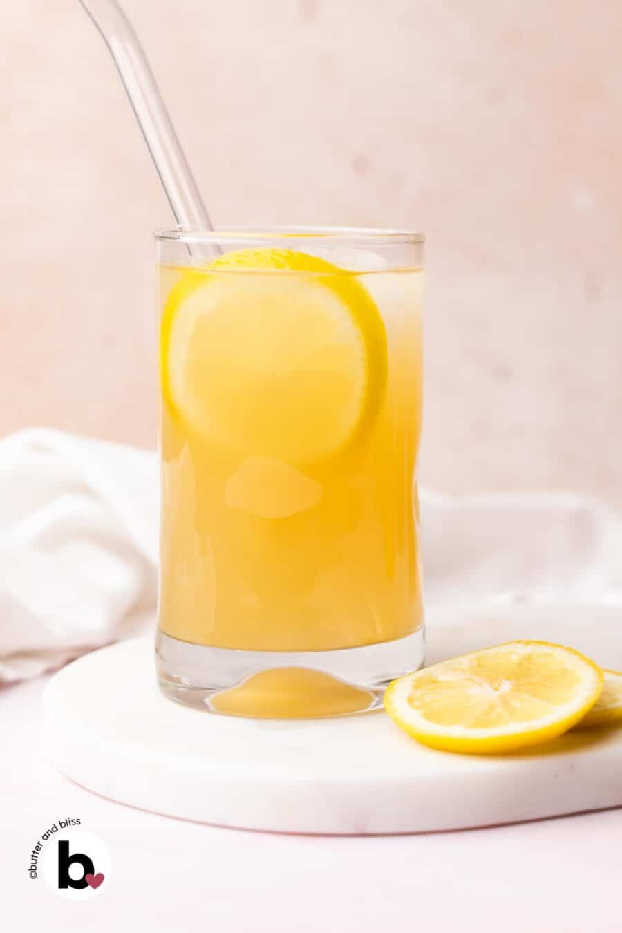 A glass of homemade ginger lemonade with lemon slice garnish on a marble plate.
