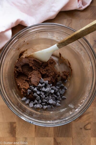 Chocolate cookie dough in a mixing bowl with chocolate chips mixed in with a spatula.