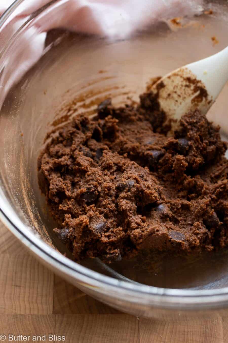 Thick double chocolate chip cookie dough in a bowl with a spatula.