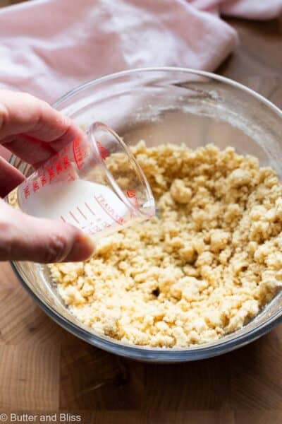 Hand pouring a small amount of milk into a bowl of cookie dough.