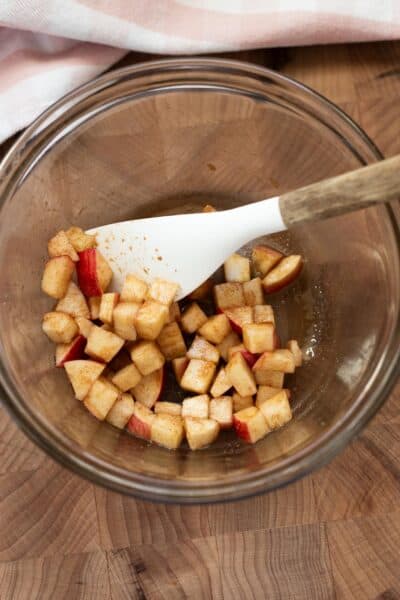 Chunks of apple soaking with sugar in a mixing bowl.