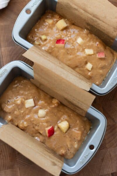 Two mini loaf pans full of apple banana bread batter with chunks of apple.