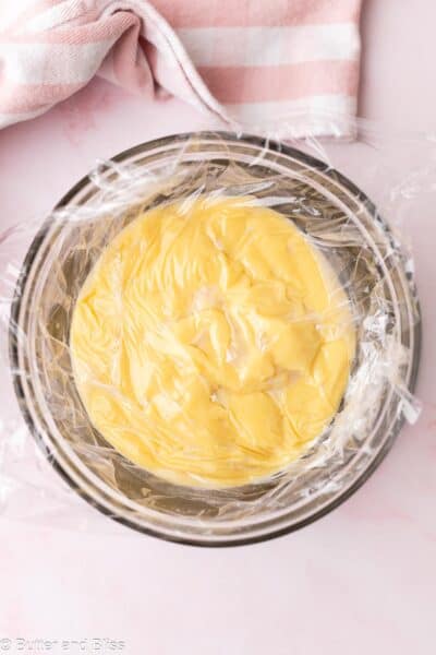 Vanilla pudding in a mixing bowl covered with plastic wrap.
