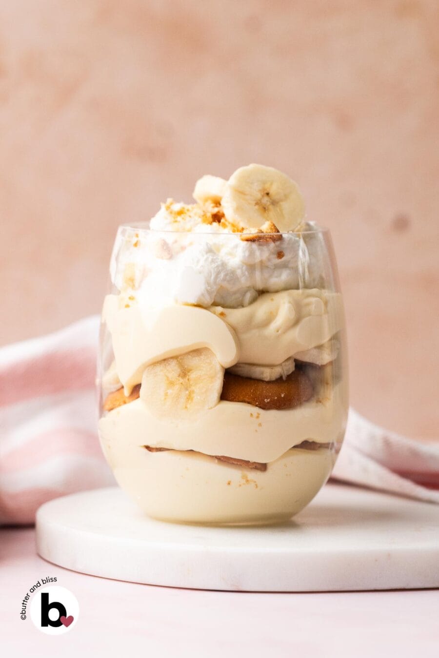 Individual banana pudding cup with layers of pudding, bananas, wafers, and whipped cream.