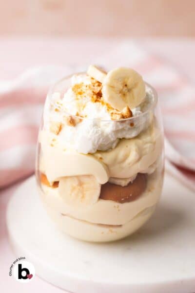 A single parfait glass of banana pudding topped with whipped cream and fresh banana slices.