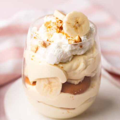 A single parfait glass of banana pudding topped with whipped cream and fresh banana slices.