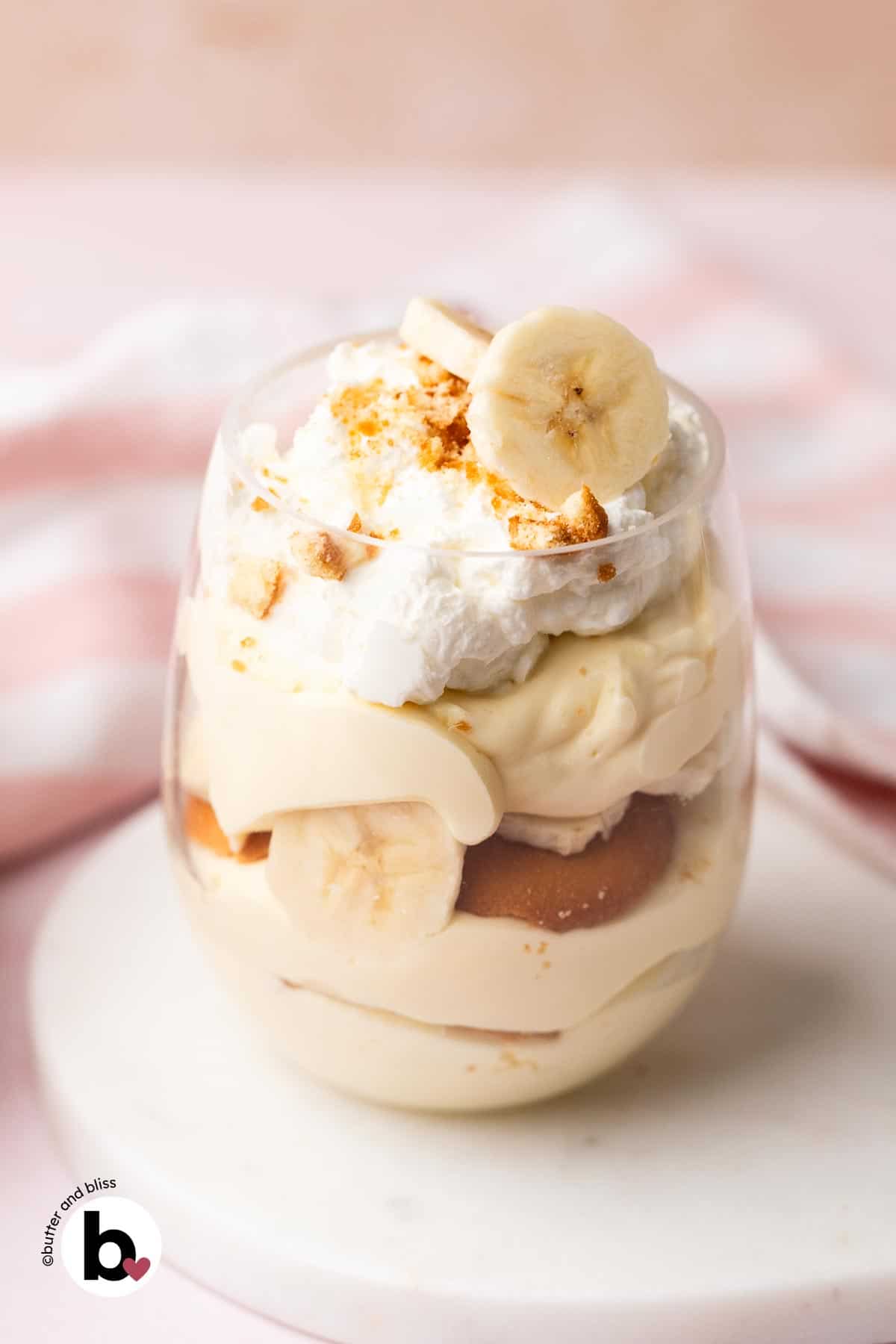 A single parfait glass of banana pudding topped with whipped cream and fresh banana slices.