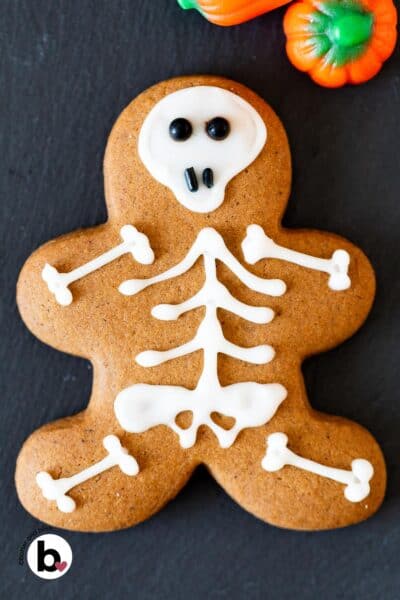 Gingerbread man cookie decorated with icing like a cute skeleton on a black plate.