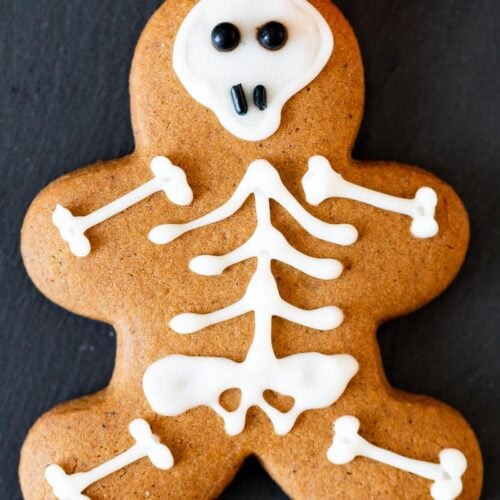 Gingerbread man cookie decorated with icing like a cute skeleton on a black plate.