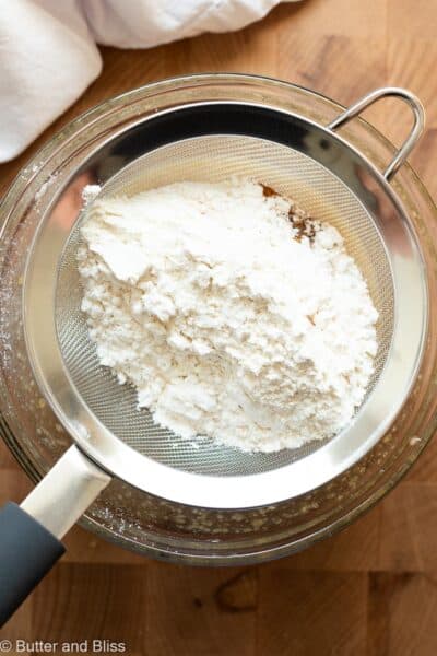 Flour being sifted into a bowl next to a white napkin.