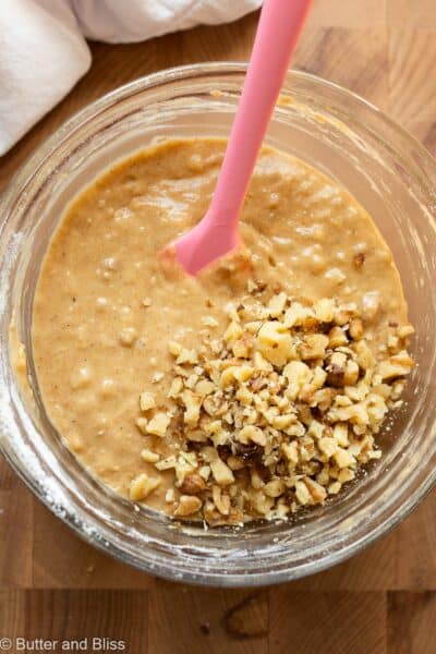 Banana muffin batter in a bowl with added walnuts, next to a white napkin.