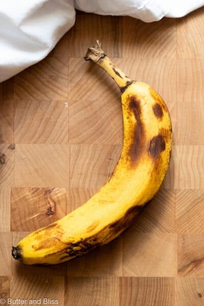 A single spotty, perfectly ripe banana on a wood cutting board next to a white napkin.