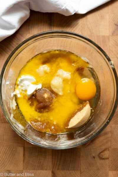 A mixing bowl on a wood cutting board full of mashed banana and other wet ingredients to make muffins.
