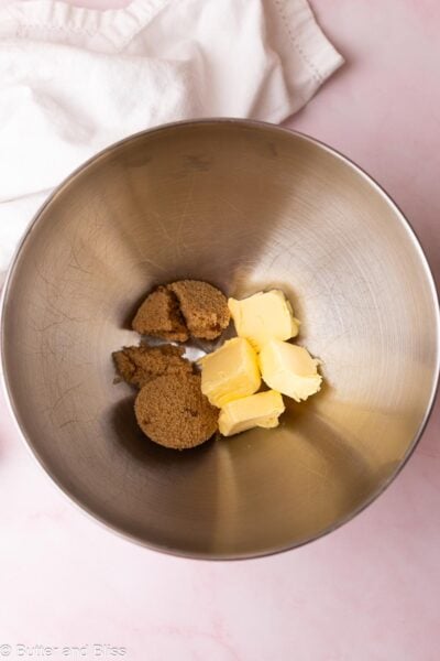 Butter cubes and brown sugar in a metal mixing bowl next to a white napkin.