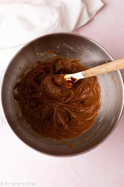 Molasses mixed into butter and sugar in a metal mixing bowl.