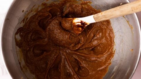 Molasses mixed into butter and sugar in a metal mixing bowl.