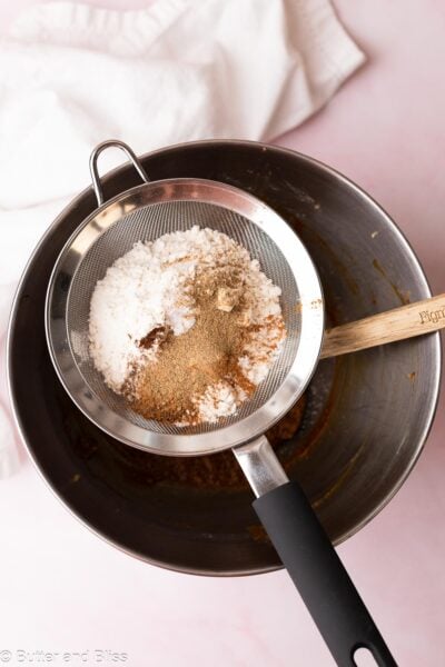 Mesh strainer full of flour and spices set over a metal mixing bowl.