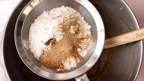 Mesh strainer full of flour and spices set over a metal mixing bowl.