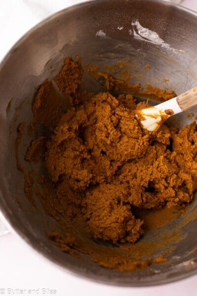 Thick and sticky gingerbread cookie dough in a metal mixing bowl with a spatula.