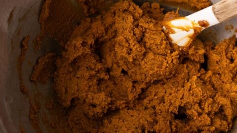 Thick and sticky gingerbread cookie dough in a metal mixing bowl with a spatula.