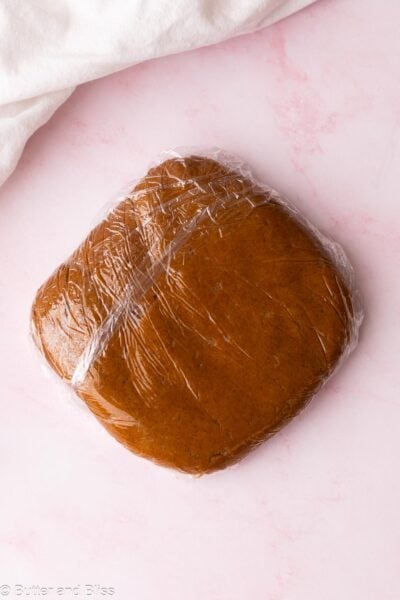 Gingerbread cookie dough shaped into a disc and wrapped in plastic wrap on a table.