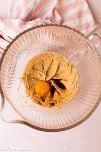 Creamed butter and sugar with an egg yolk in a clear mixing bowl next to a pink checkered napkin.