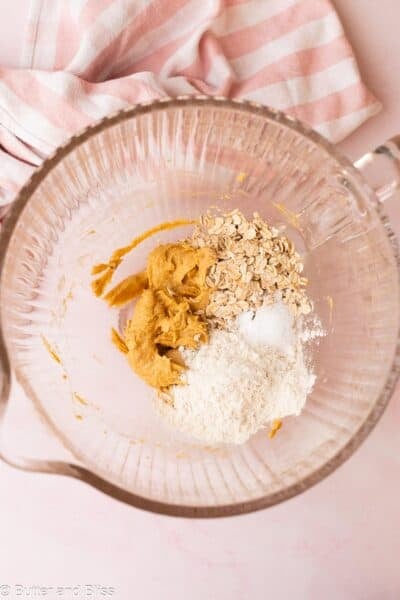 Flour and oats added to creamed butter in a clear mixing bowl next to pink napkin.