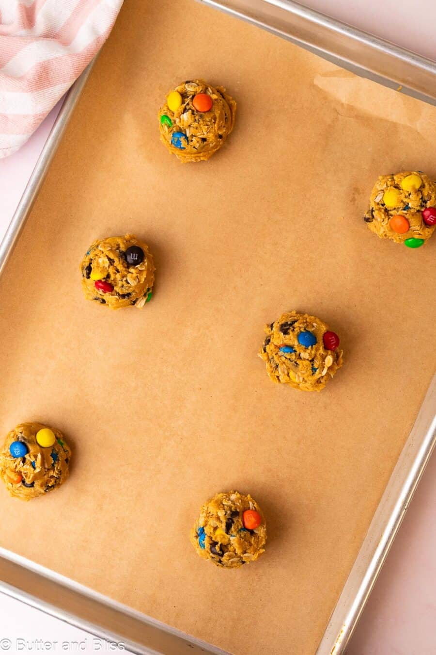 Monster cookie dough balls on a parchment lined baking sheet.
