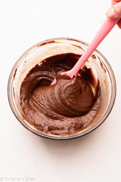 Thick brownie batter being mixed in a bowl with a pink spatula.