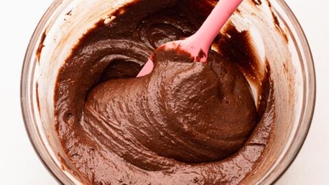 Thick brownie batter being mixed in a bowl with a pink spatula.