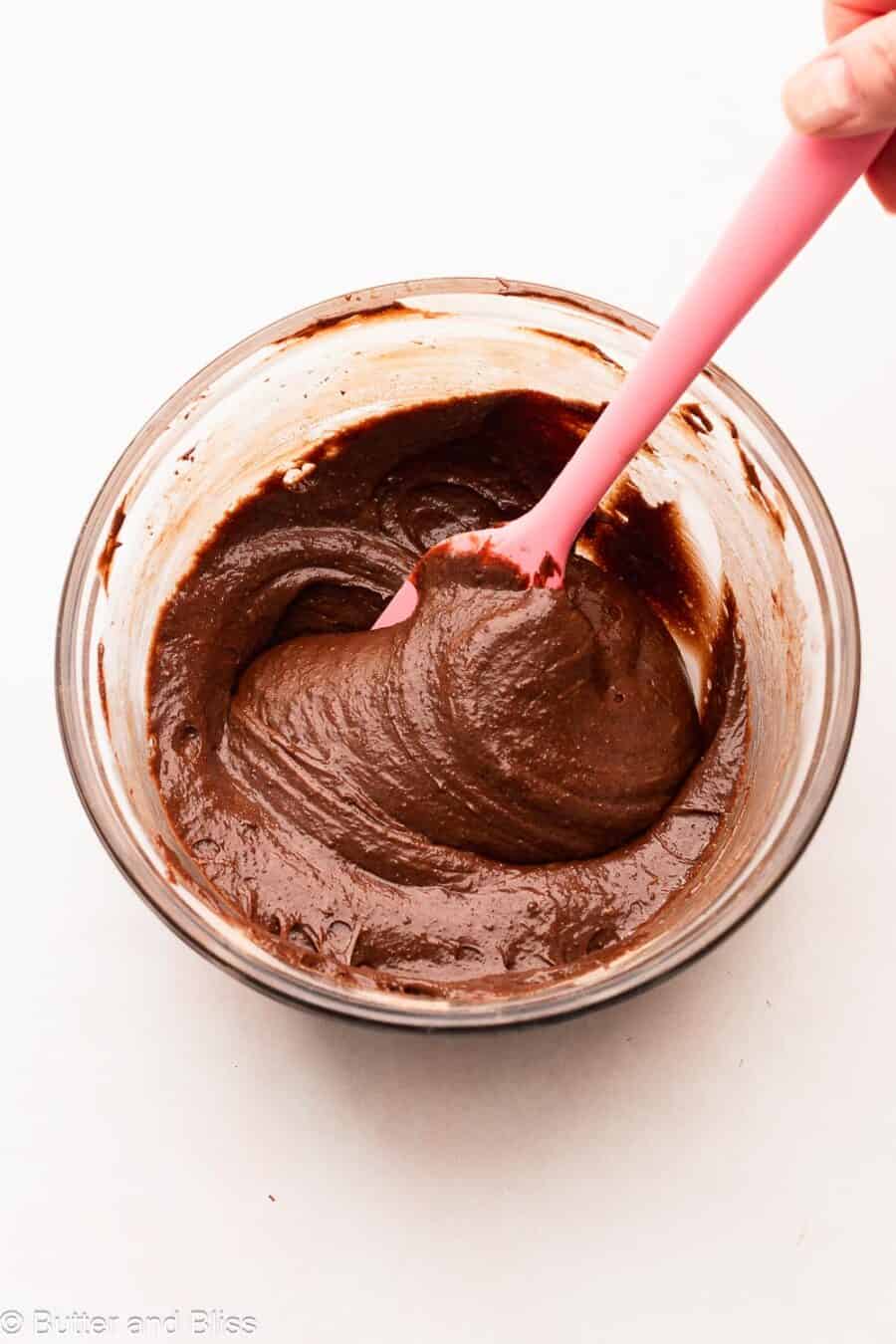 Thick brownie batter being mixed in a bowl with a pink spatula.