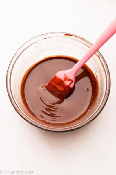 Smooth melted chocolate in a small mixing bowl with a pink spatula.