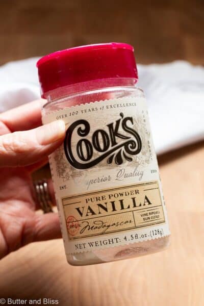 Hand holding a small jar of vanilla powder.