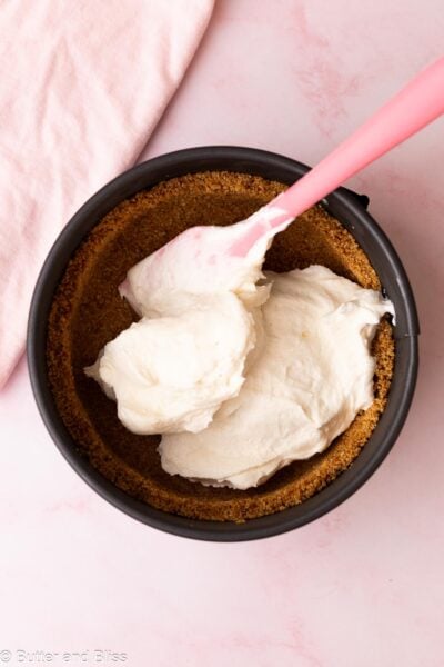 Cheesecake filling being dolloped into a graham cracker crust in a small springform pan.
