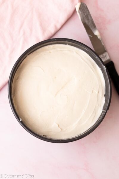 No-bake cheesecake filling smoothed out with an offset spatula after being added to the crust in the springform pan.